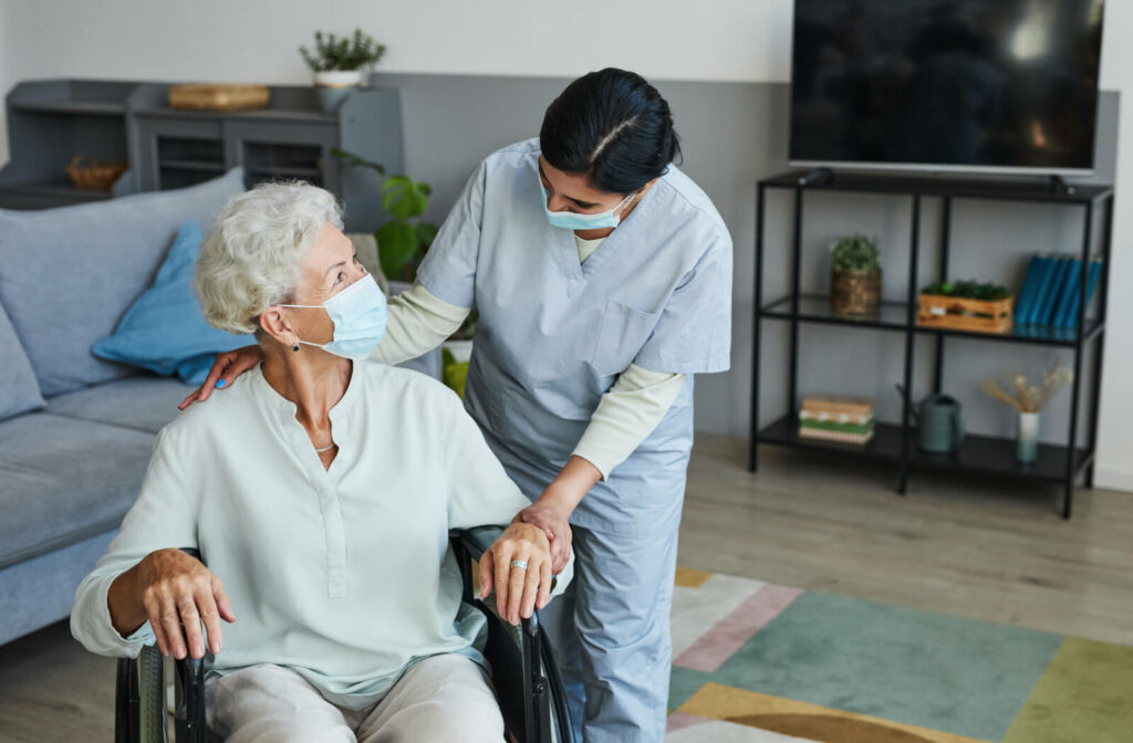 A female nurse is assisting a senior woman in a wheelchair to move in the living room.