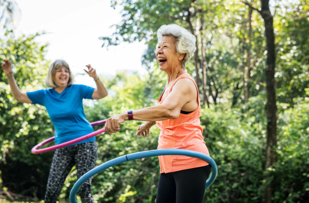 Two senior women exercising with a hula hoop outdoors.