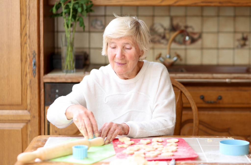 A senior woman is molding cookie dough while seated.