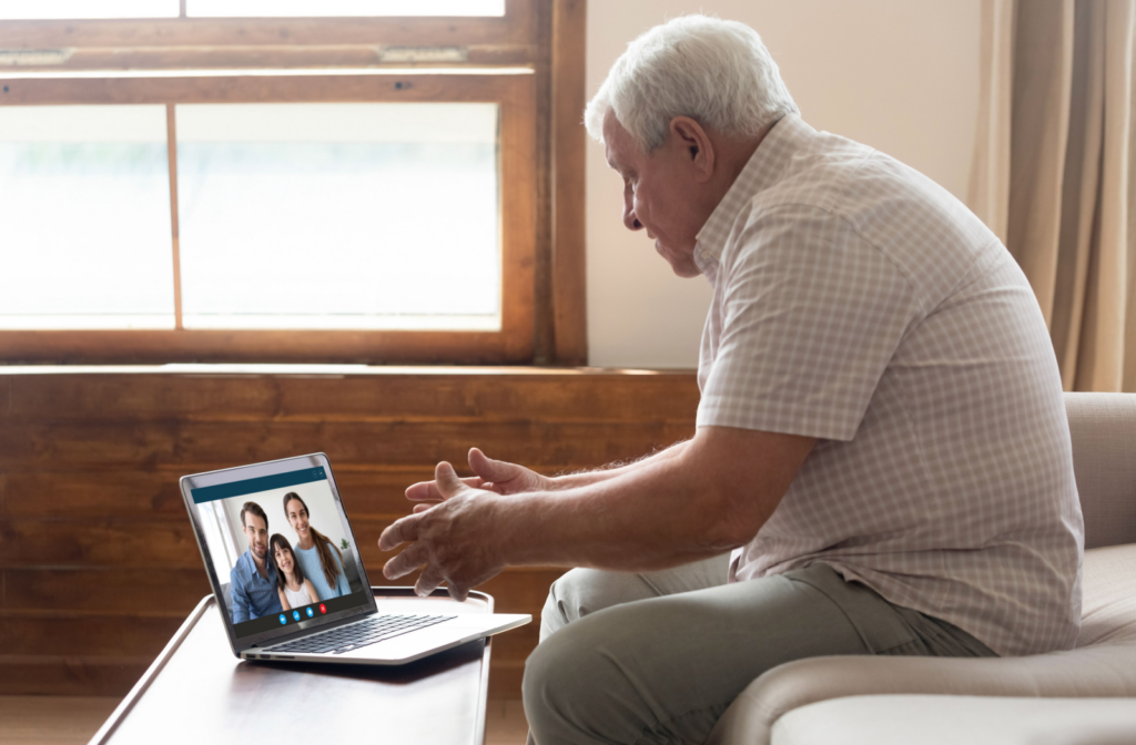 A senior man in a checkered shirt video-calling his loved ones using a laptop to keep in touch with them.