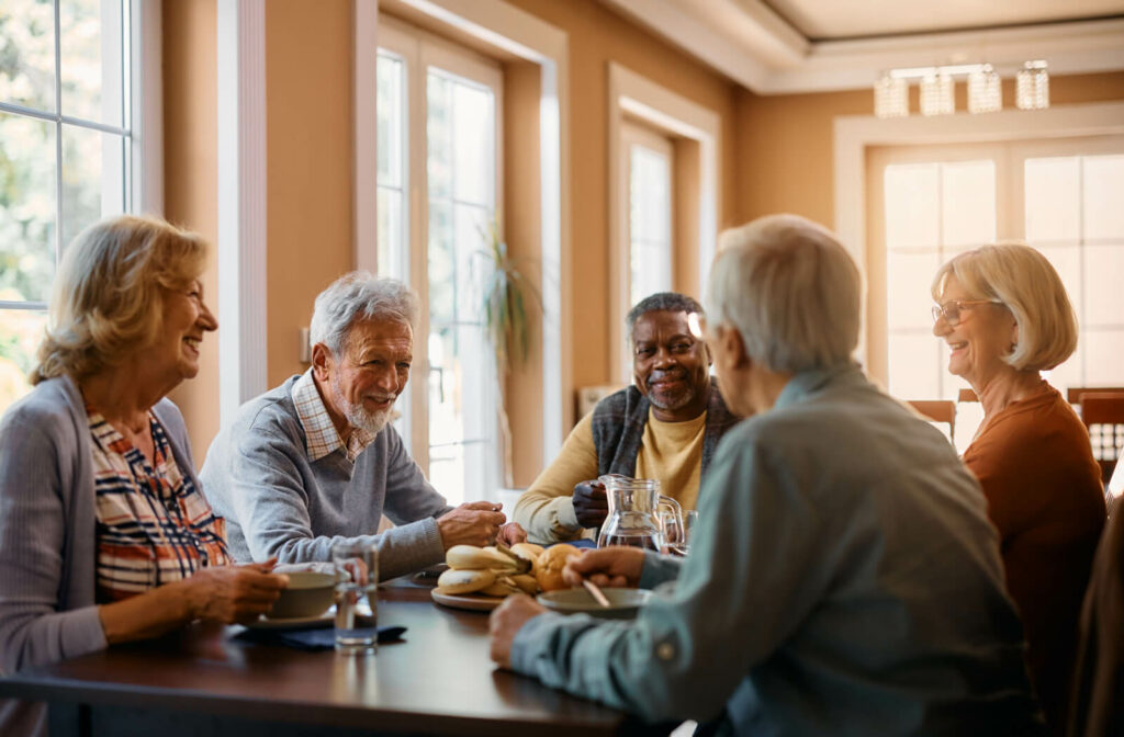 A group of older adults sitting around a table, eating and enjoying breakfast while smiling and chatting with each other